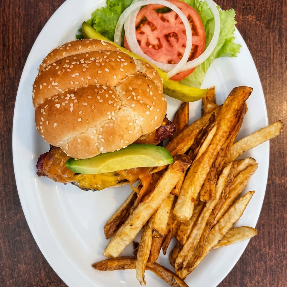 A cheeseburger with avocado, lettuce, tomato, onion, and pickles, served with a side of fries.