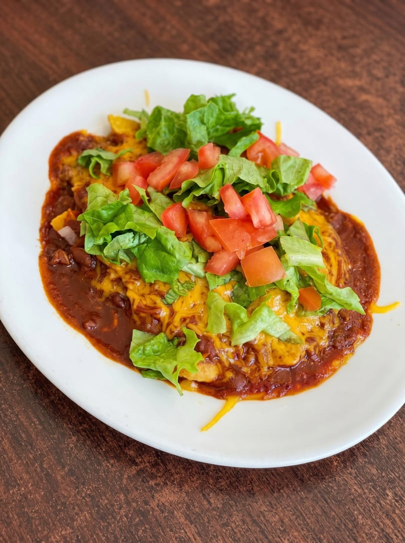 A plate of enchiladas covered in chili, melted cheese, lettuce, and diced tomatoes.
